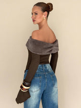 A woman shown from the back wearing a dark brown off-the-shoulder long-sleeve top with a wide fuzzy taupe-gray collar, paired with blue jeans and stacked bracelets, against a plain beige background.