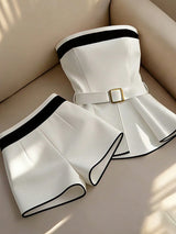 White outfit with black trim and a gold belt on a beige surface