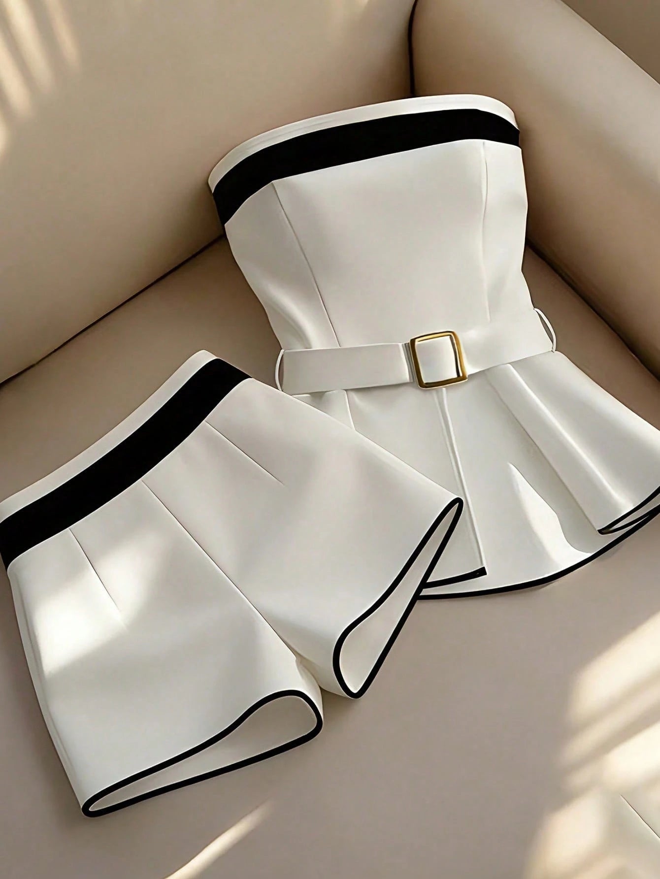 White outfit with black trim and a gold belt on a beige surface