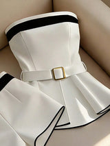 White dress with black trim and gold buckle on a beige surface