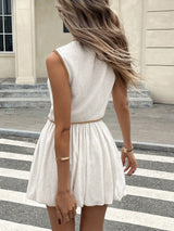 Woman wearing a white dress with a beige belt on a city street.
