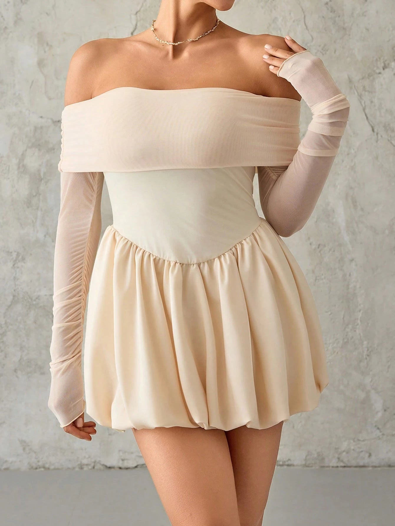 Woman wearing a beige off-shoulder top and skirt with sheer sleeves against a gray background