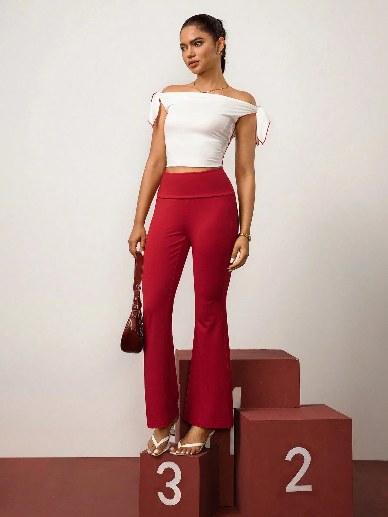 Woman in white off-shoulder top and red high-waisted pants standing on a podium with numbers.
