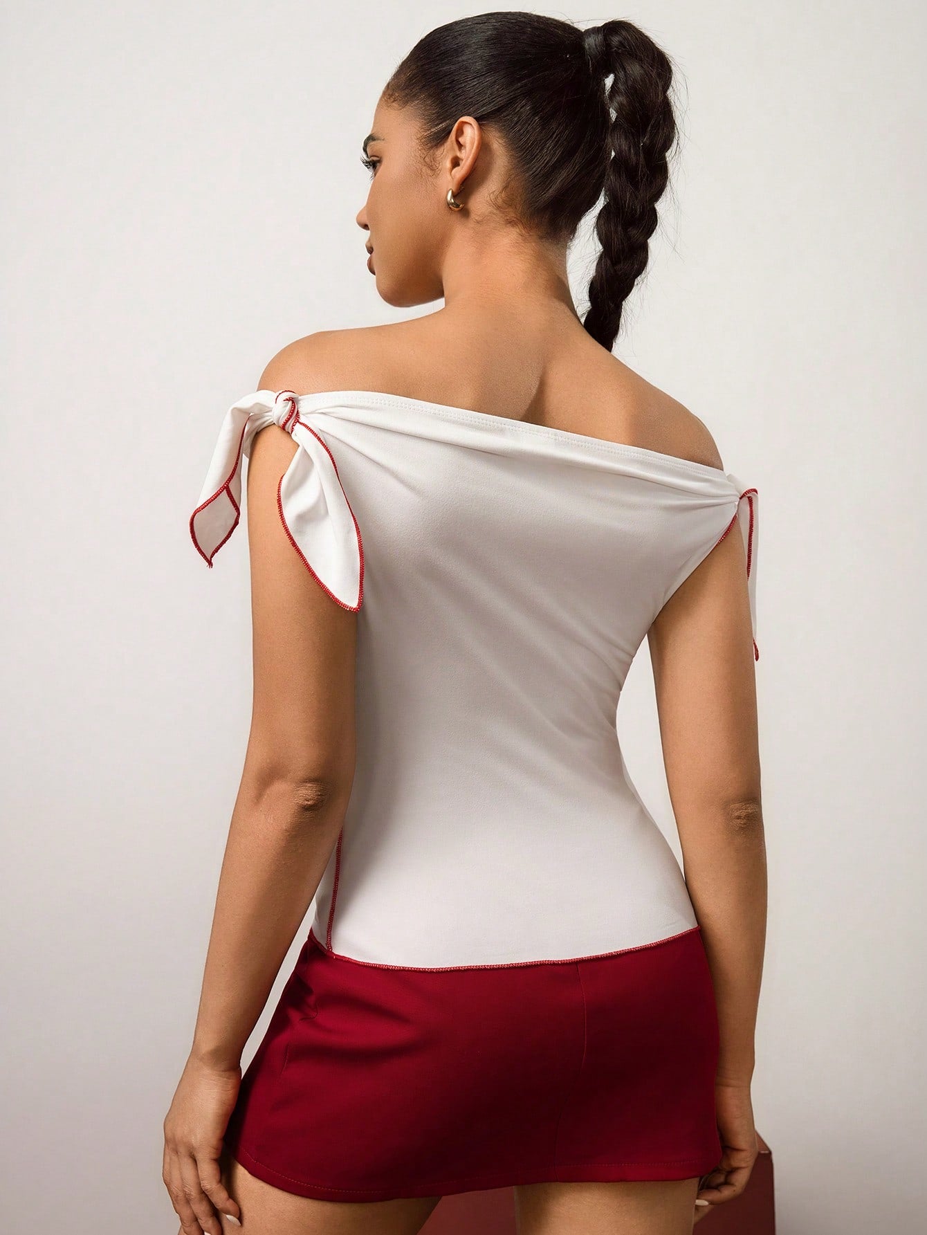 Woman wearing a white off-shoulder top with red accents and a red skirt on a plain background