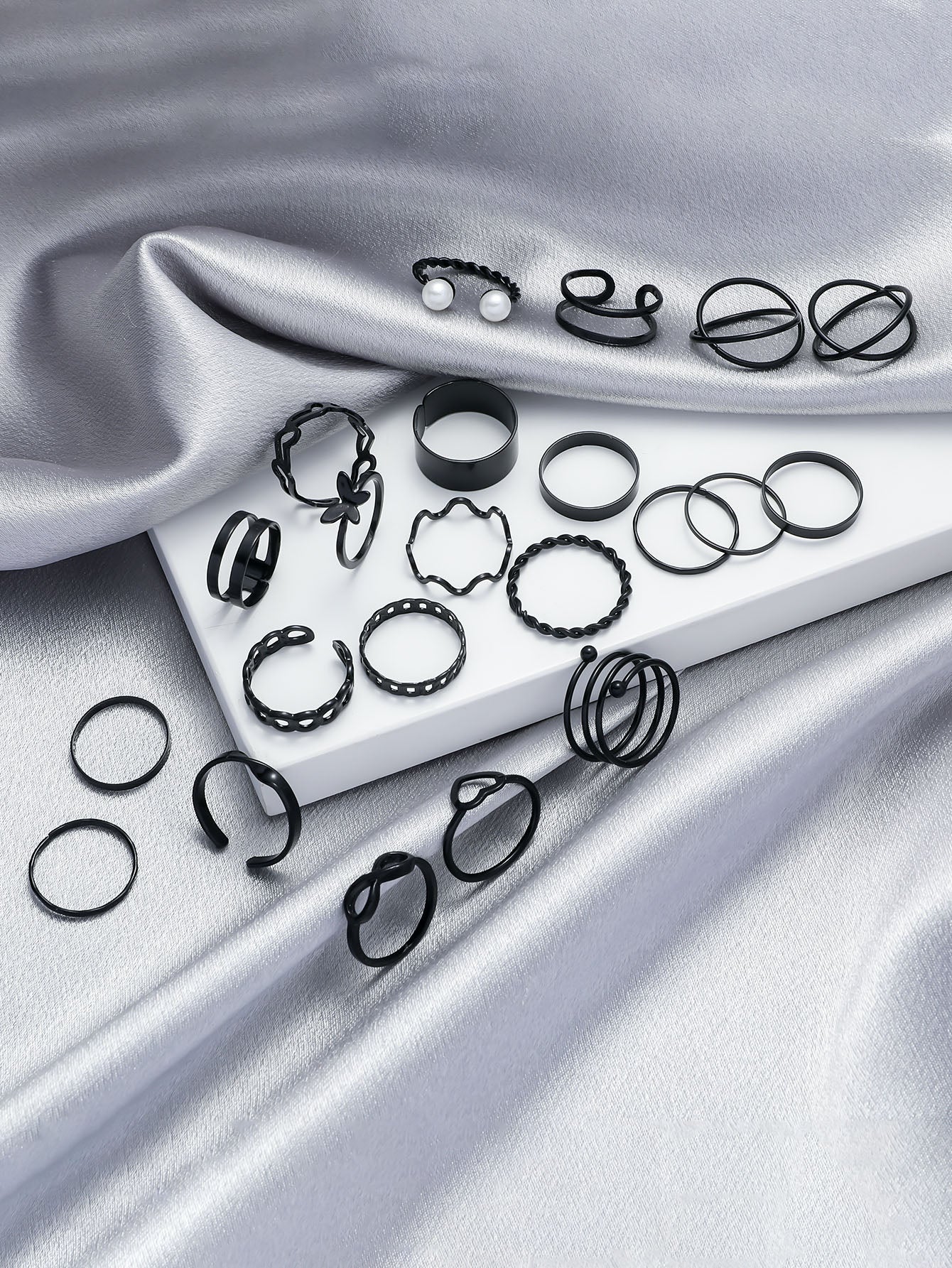 Black rubber bands on a white tray with pearls, placed on silver fabric.