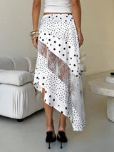 Person wearing a white skirt with black polka dots and lace in a minimalistic room.