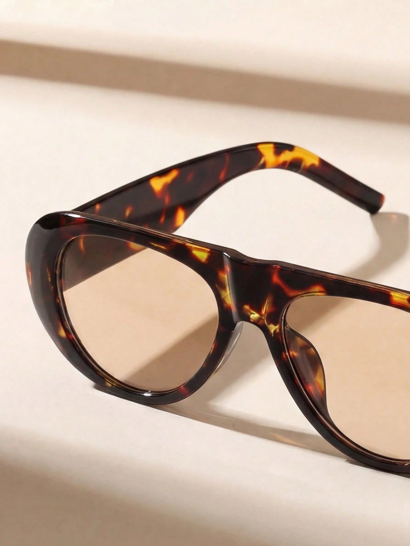 Tortoiseshell sunglasses with brown lenses on a light beige background