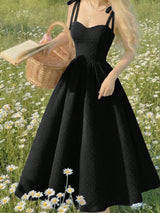 Woman in a black dress holding a basket and book in a field of flowers