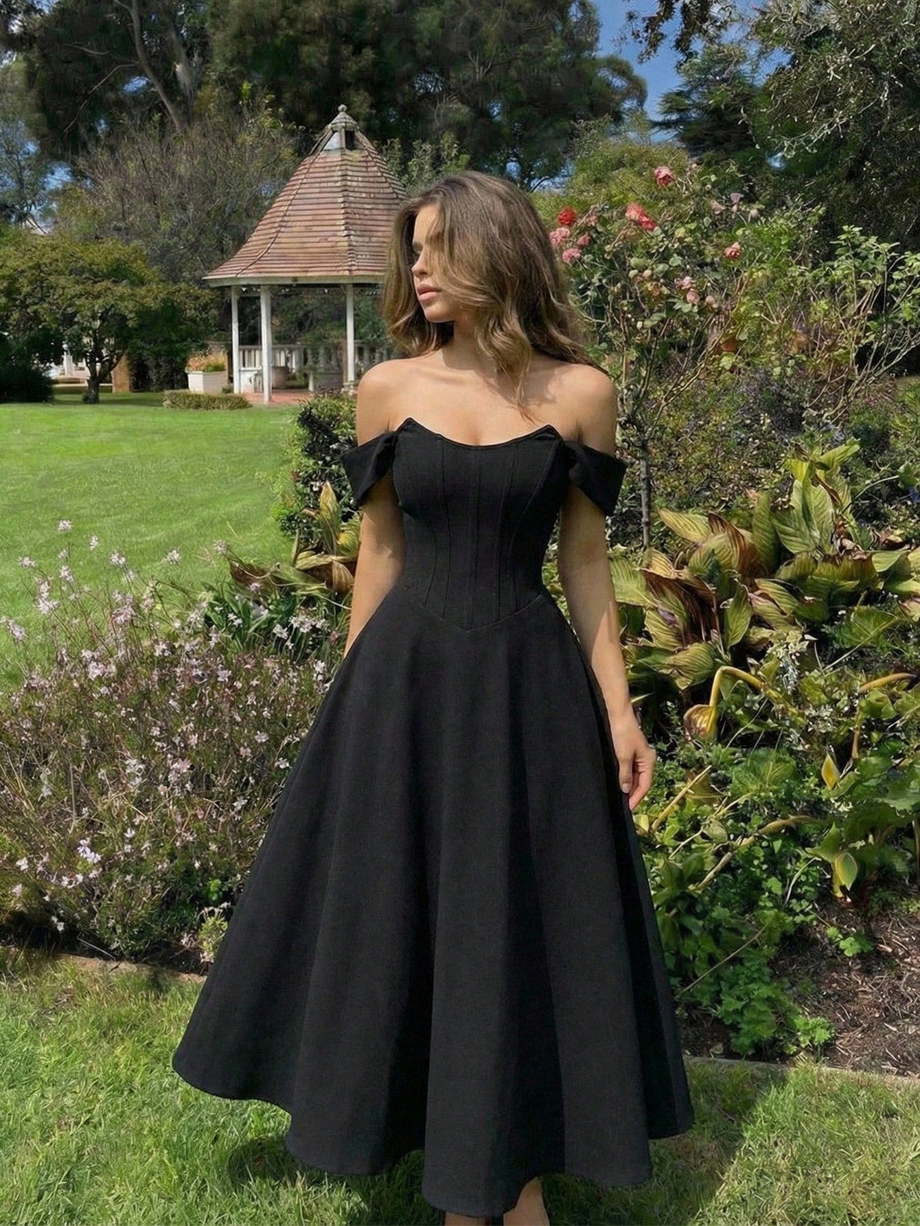 Woman wearing a black off-shoulder dress in a garden setting