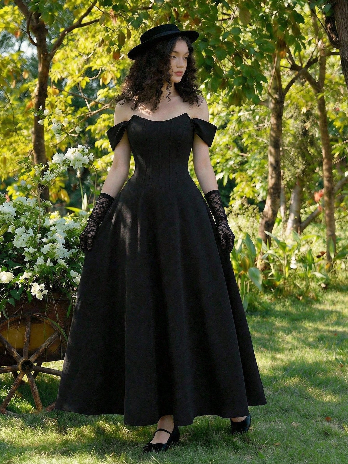 Woman in a black dress standing in a garden with trees and flowers.