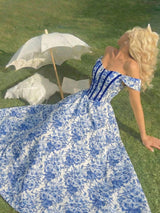 Woman in a blue floral dress lying on grass with an umbrella nearby
