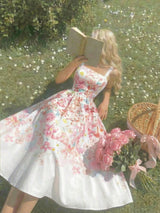 Woman in a floral dress holding a book and flowers in a garden