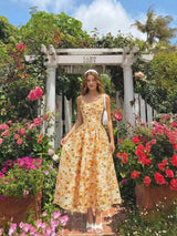 Woman in a floral dress standing in a garden with flowers and a white archway in the background.