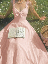 Woman in a pink dress sitting on grass with an open book