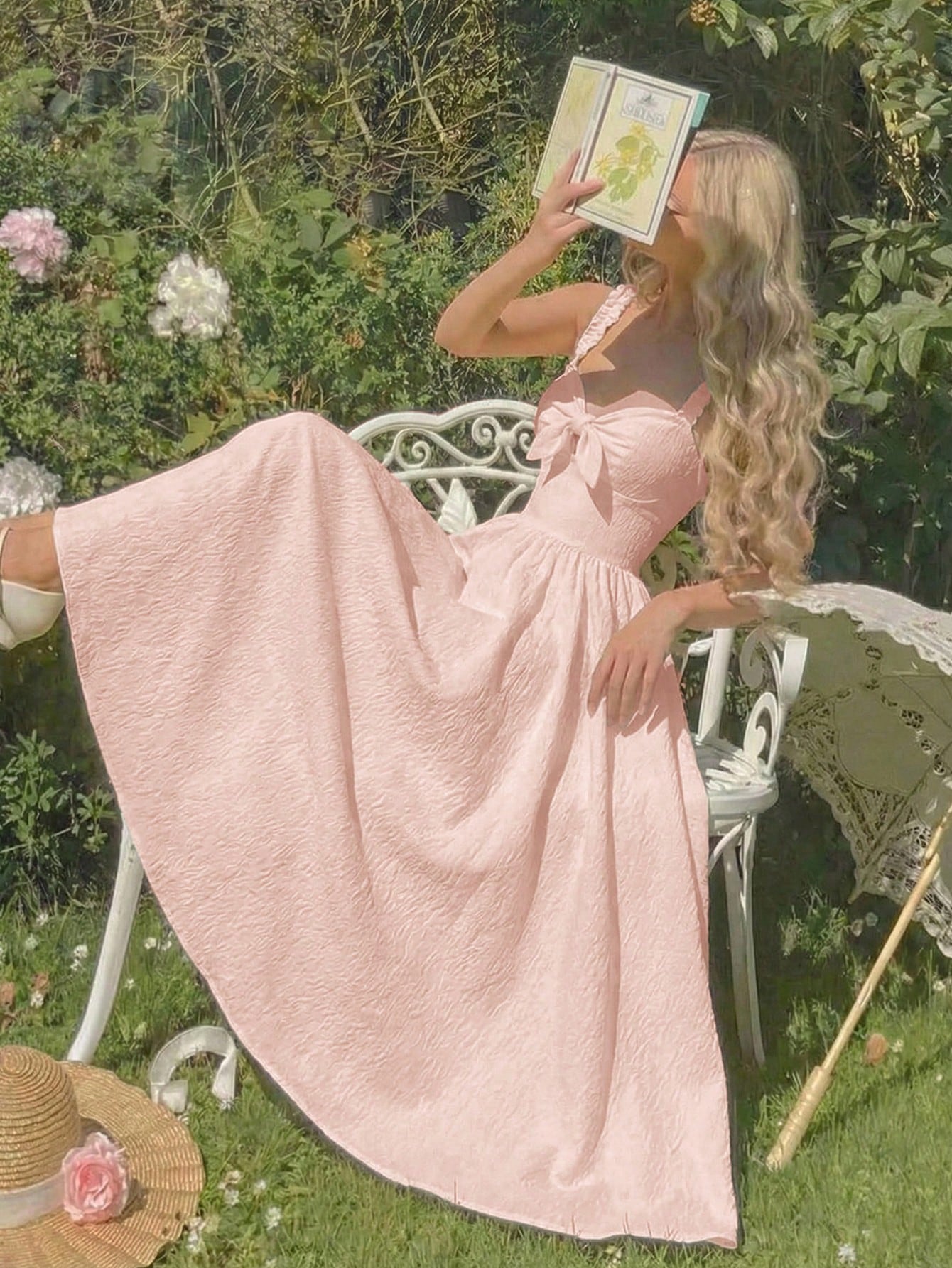 Woman in a pink dress sitting outdoors with a book, surrounded by nature.