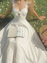 Woman in a white dress with a large bow standing in a grassy field holding an open book.