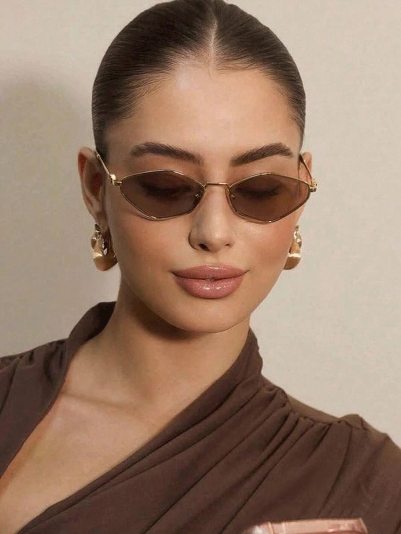 Woman wearing brown sunglasses and matching outfit against a beige background