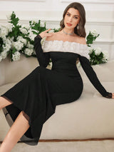 A woman models a black off-the-shoulder midi dress with a textured white yoke and sheer black long sleeves, sitting on a beige sofa with white flowers in the background.