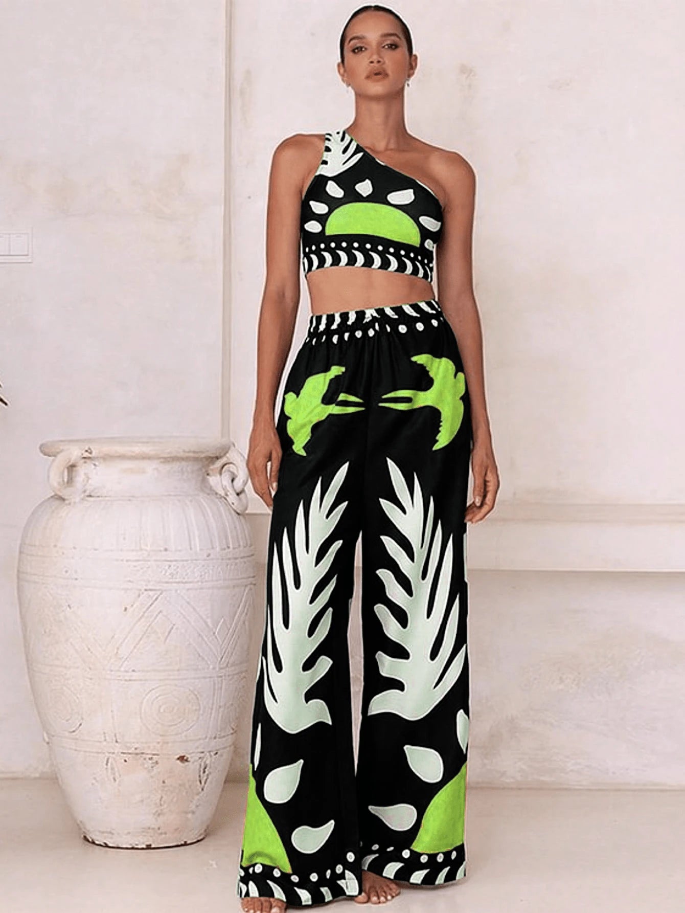 Woman wearing a black and white patterned outfit with green accents, standing next to a white vase.