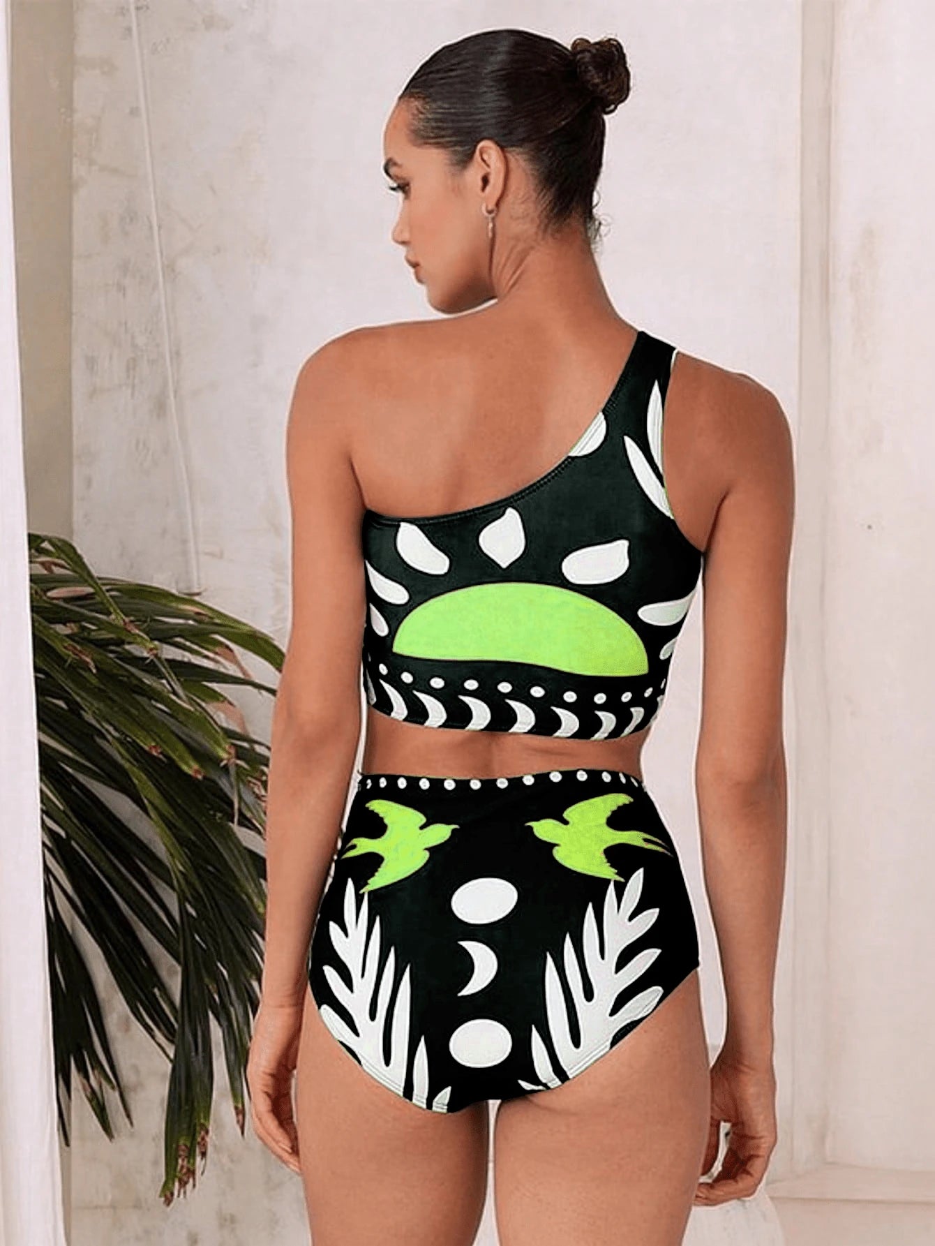Woman wearing a black and green patterned two-piece swimsuit with a plant in the background.