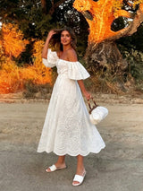 Woman in a white dress standing in front of a tree with autumn foliage.