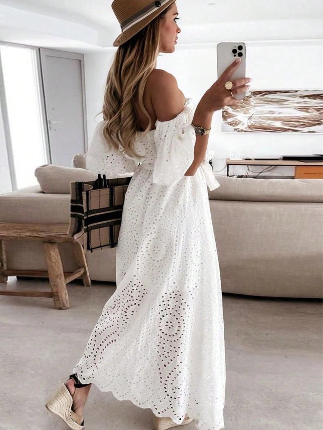 Woman in a white dress taking a selfie in a modern living room.