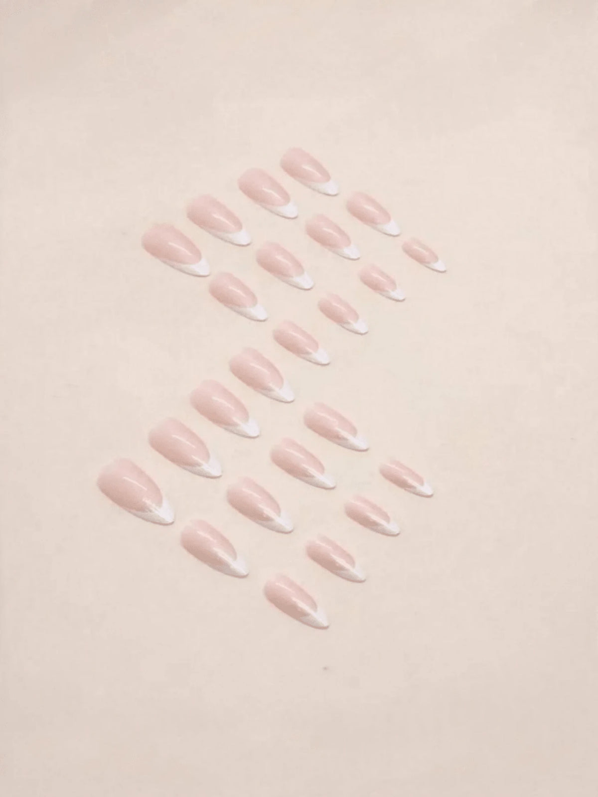 A set of false press-on nails with a pale pink nude base and white French tips, arranged in two rows on a light beige background.
