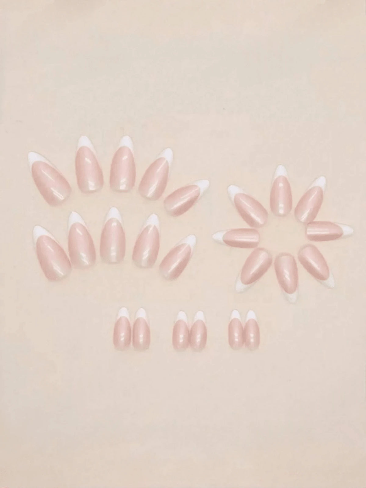 A set of false press-on nails arranged on a light beige background. The nails have a glossy pale pink body with a white French tip.