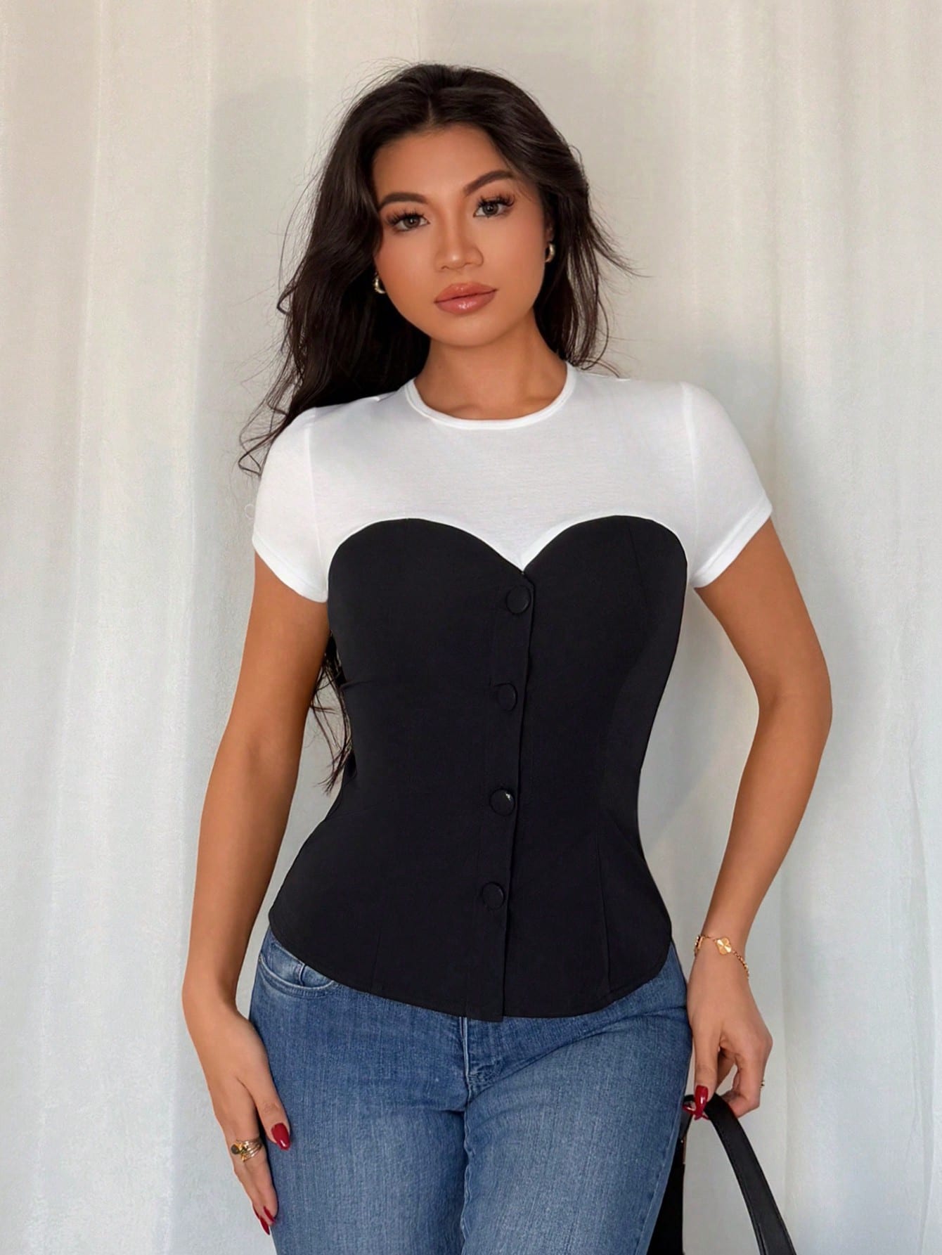 Woman wearing a black and white top with a unique design, standing against a plain background.