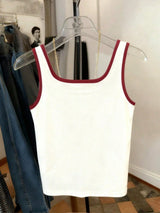 White tank top with red trim on a hanger against a neutral background