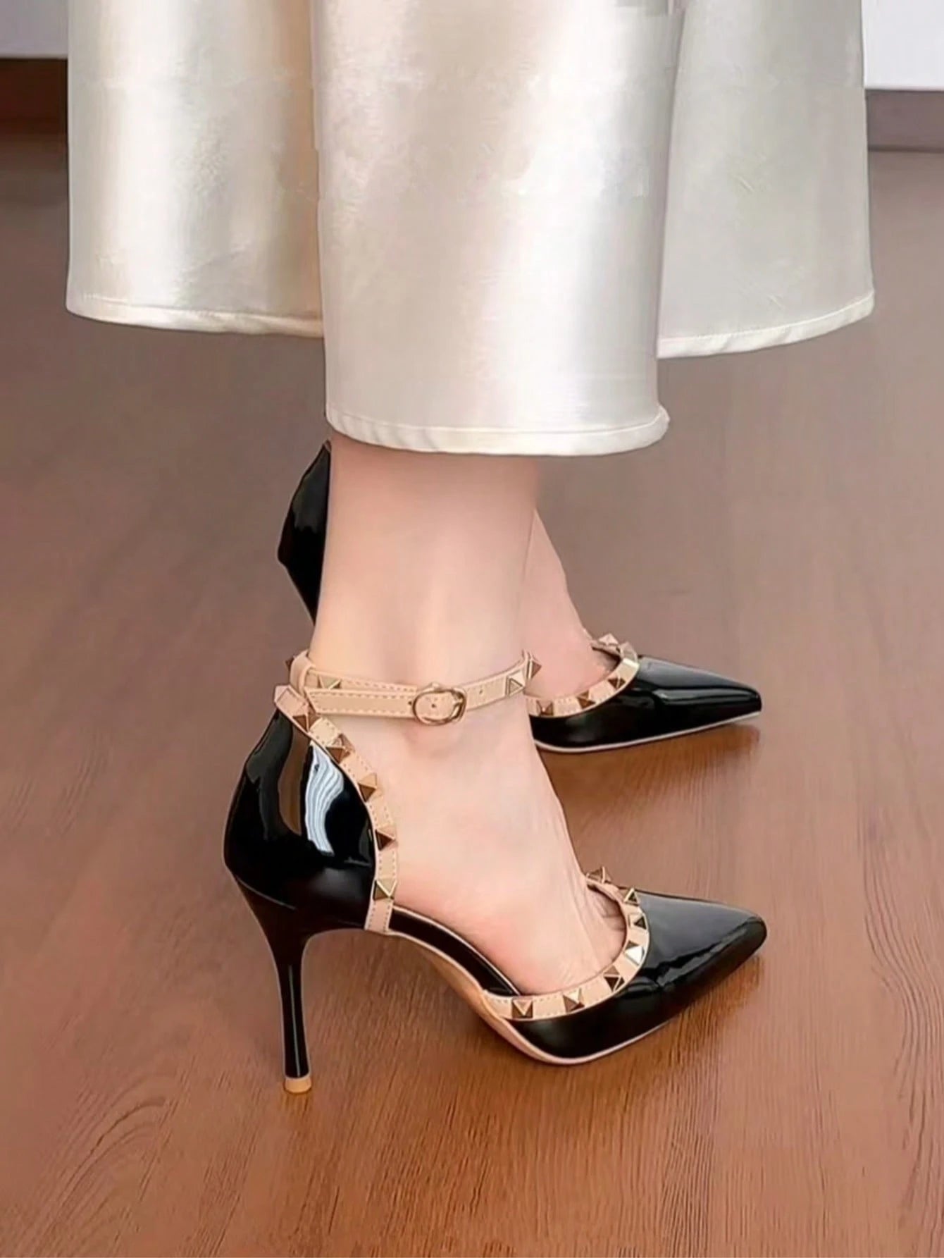 Black high-heeled shoes with gold straps worn by a person on a wooden floor.