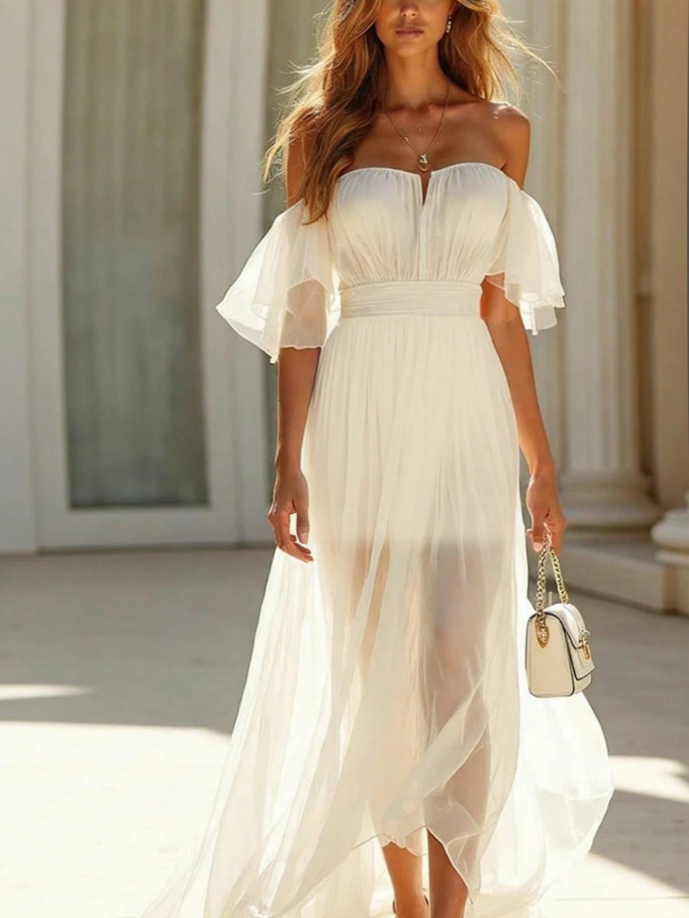 A woman wearing a flowing off-the-shoulder midi dress in a light cream or off-white color, walking outdoors near classical columns. She is holding a small white handbag.