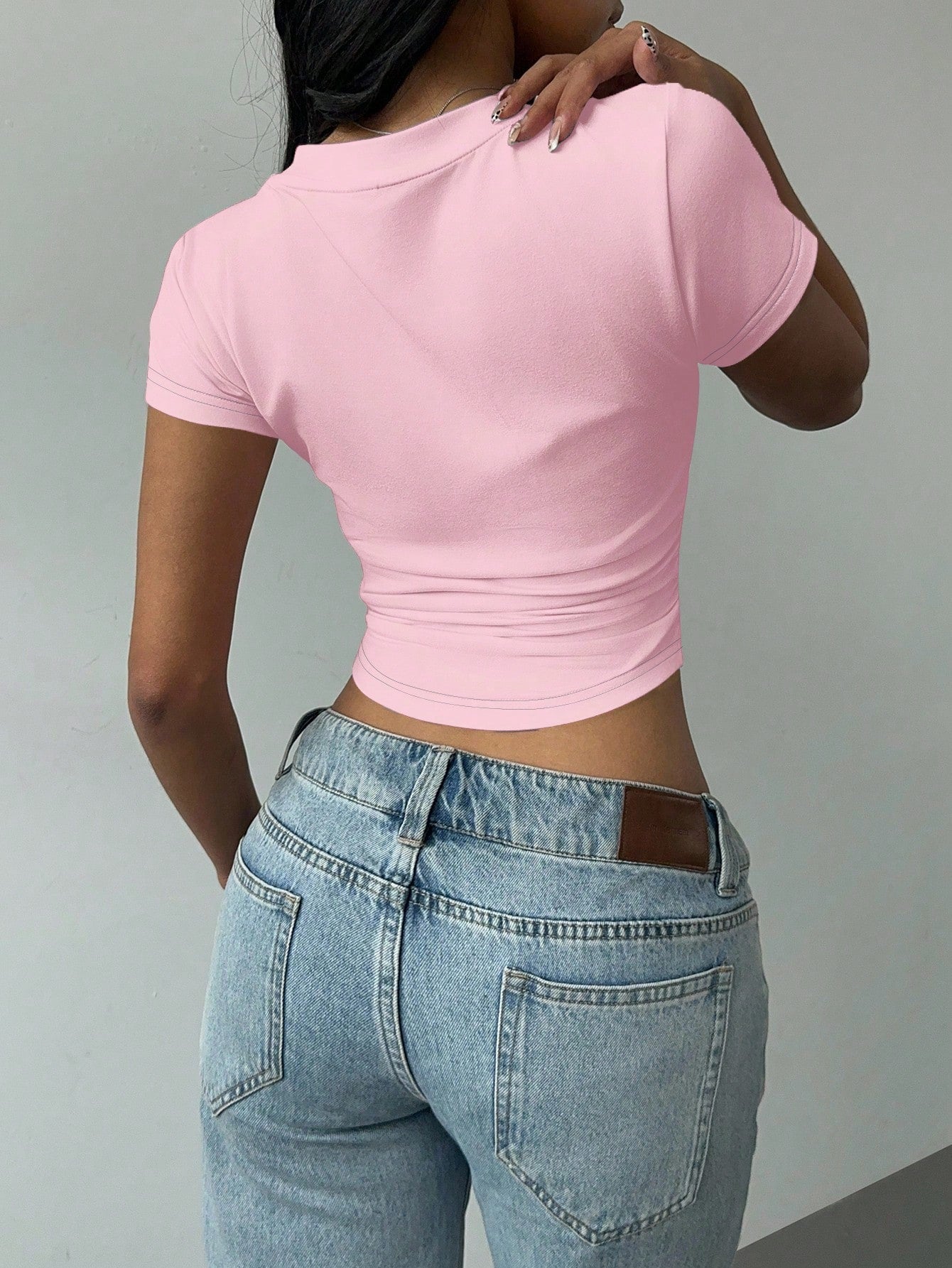 Person wearing a pink crop top and blue jeans against a gray background