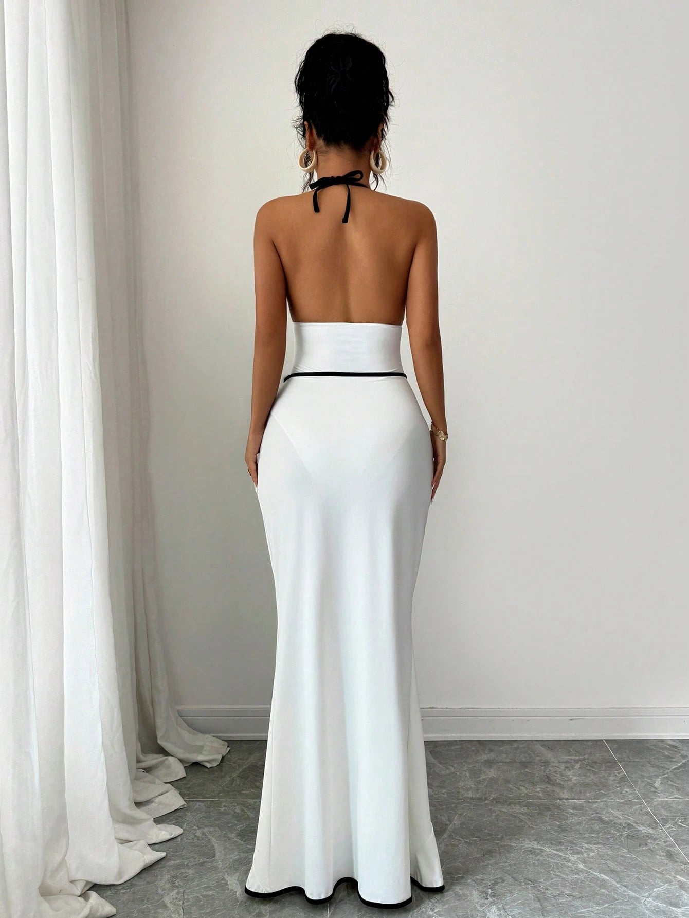 Woman wearing a white evening gown with a black belt against a plain background