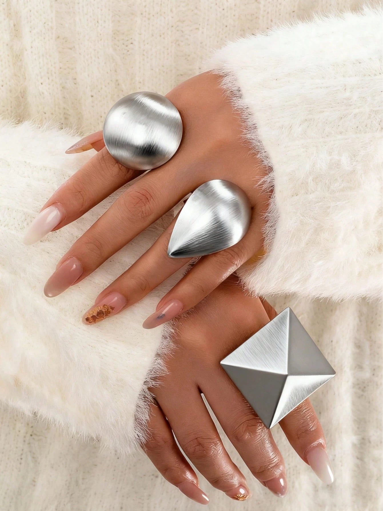 Hand wearing three silver rings on a white fur background