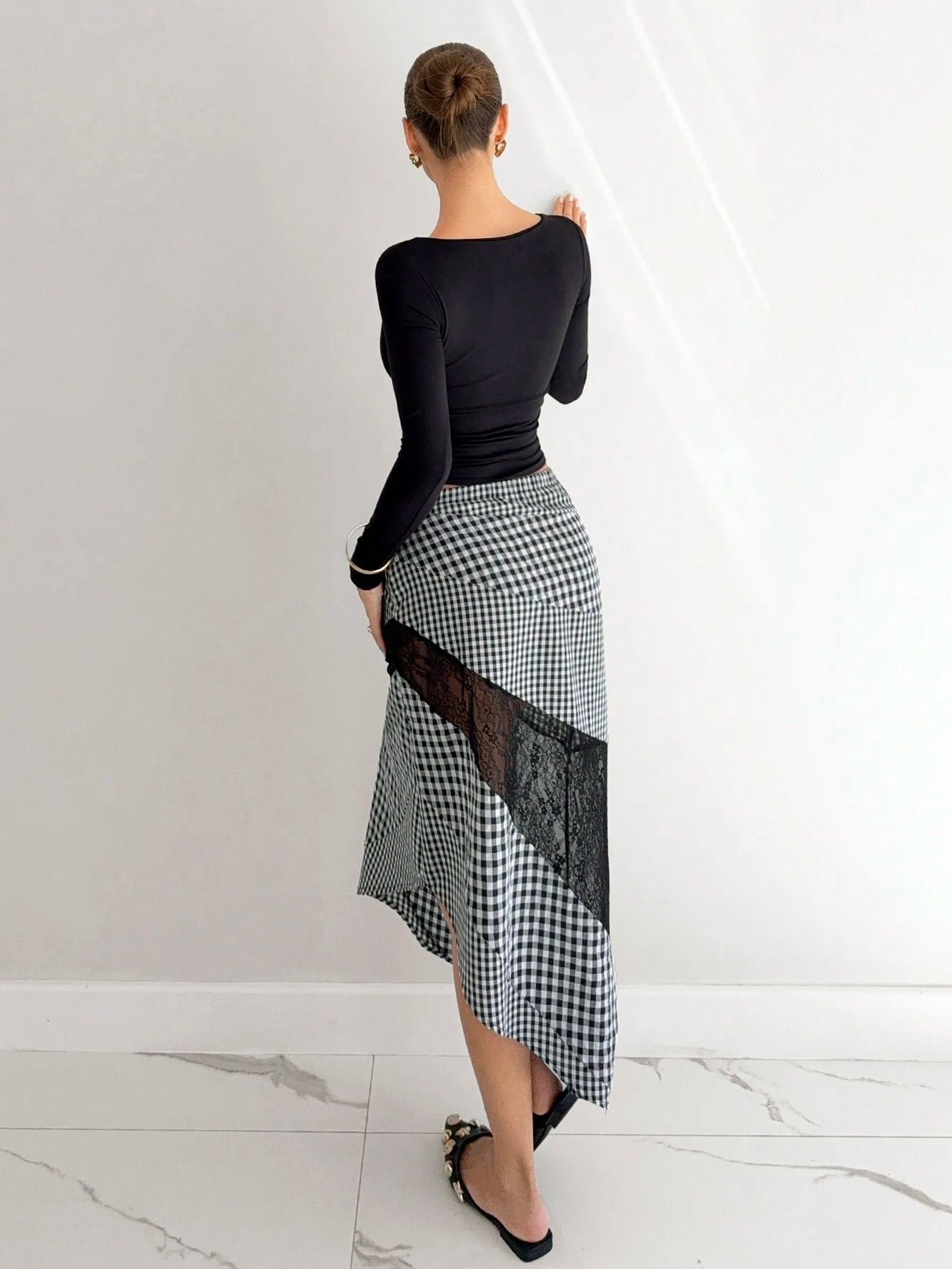 Woman wearing a black top and a checkered skirt with lace panels on a white background