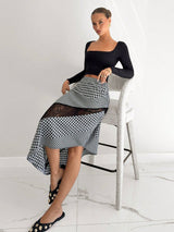 Woman wearing a black top and checkered skirt in a minimalistic setting