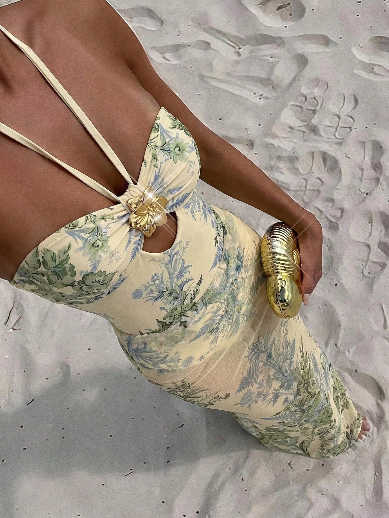 Woman in a floral dress with gold accessories on a sandy background