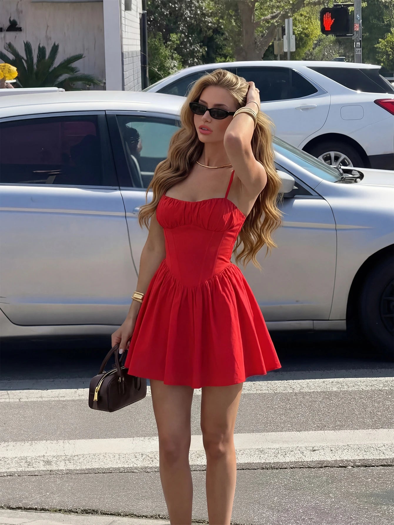 Woman in a red dress standing on a street corner with cars and traffic lights in the background.