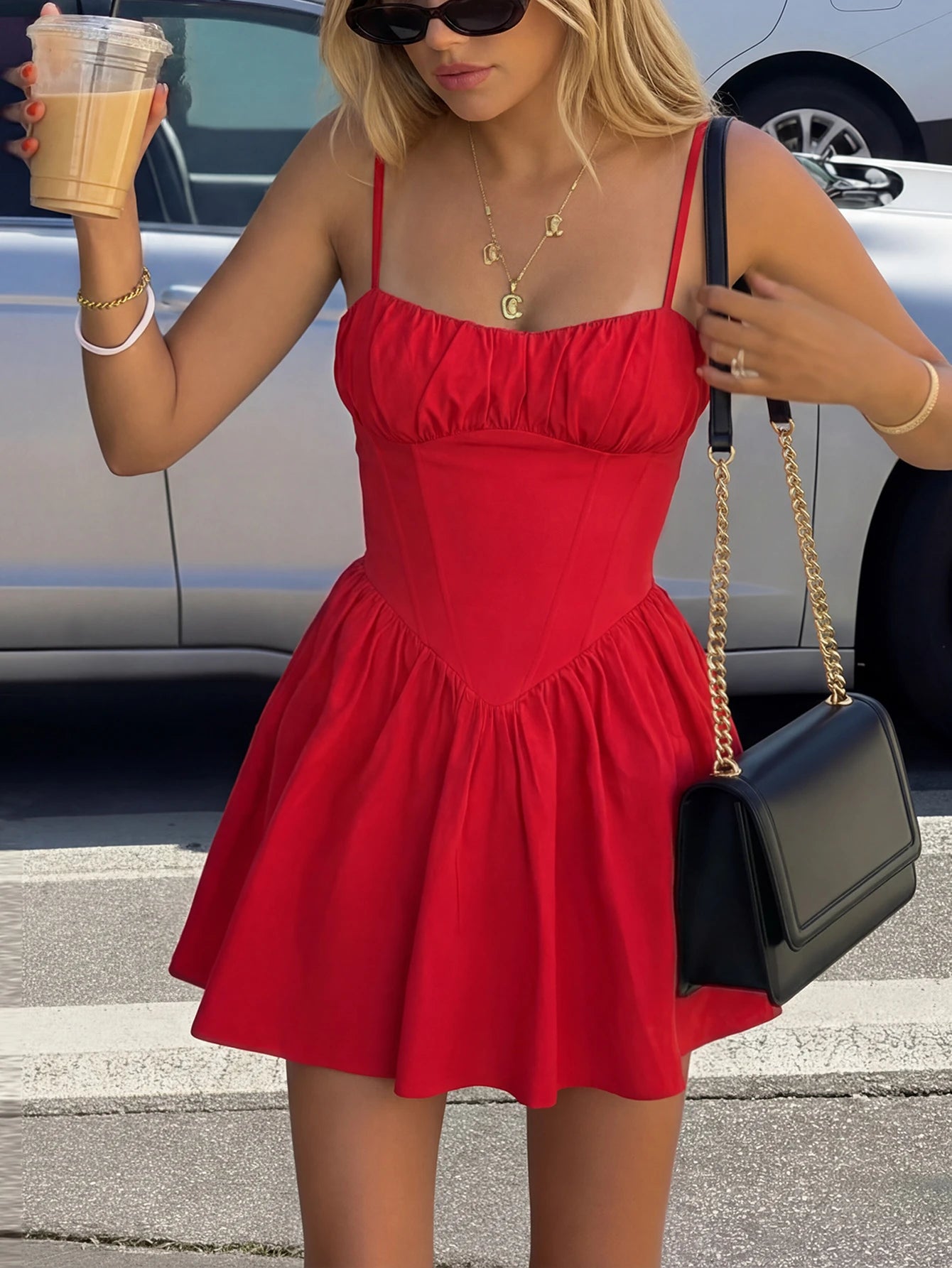 Woman in a red dress holding a drink and a black handbag on a street.