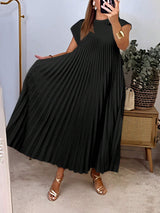 Person wearing a black pleated dress in a room with a plant and wooden cabinet.