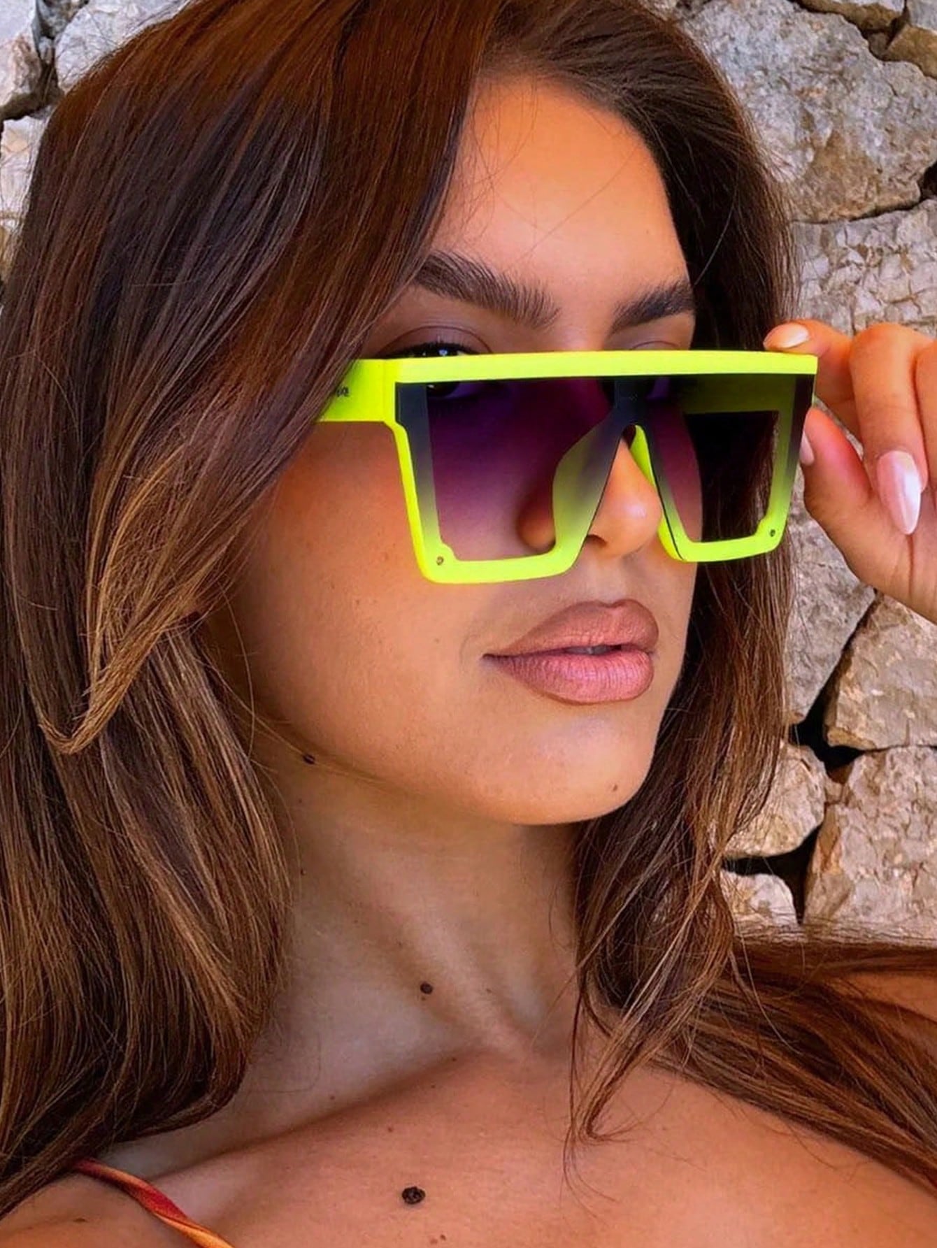 Woman wearing bright yellow sunglasses with a stone wall background