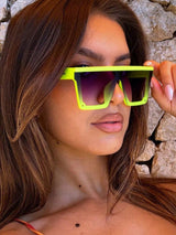 Woman wearing bright yellow sunglasses with a stone wall background