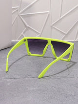 Neon green sunglasses with black lenses on a gray surface with a white geometric wall background