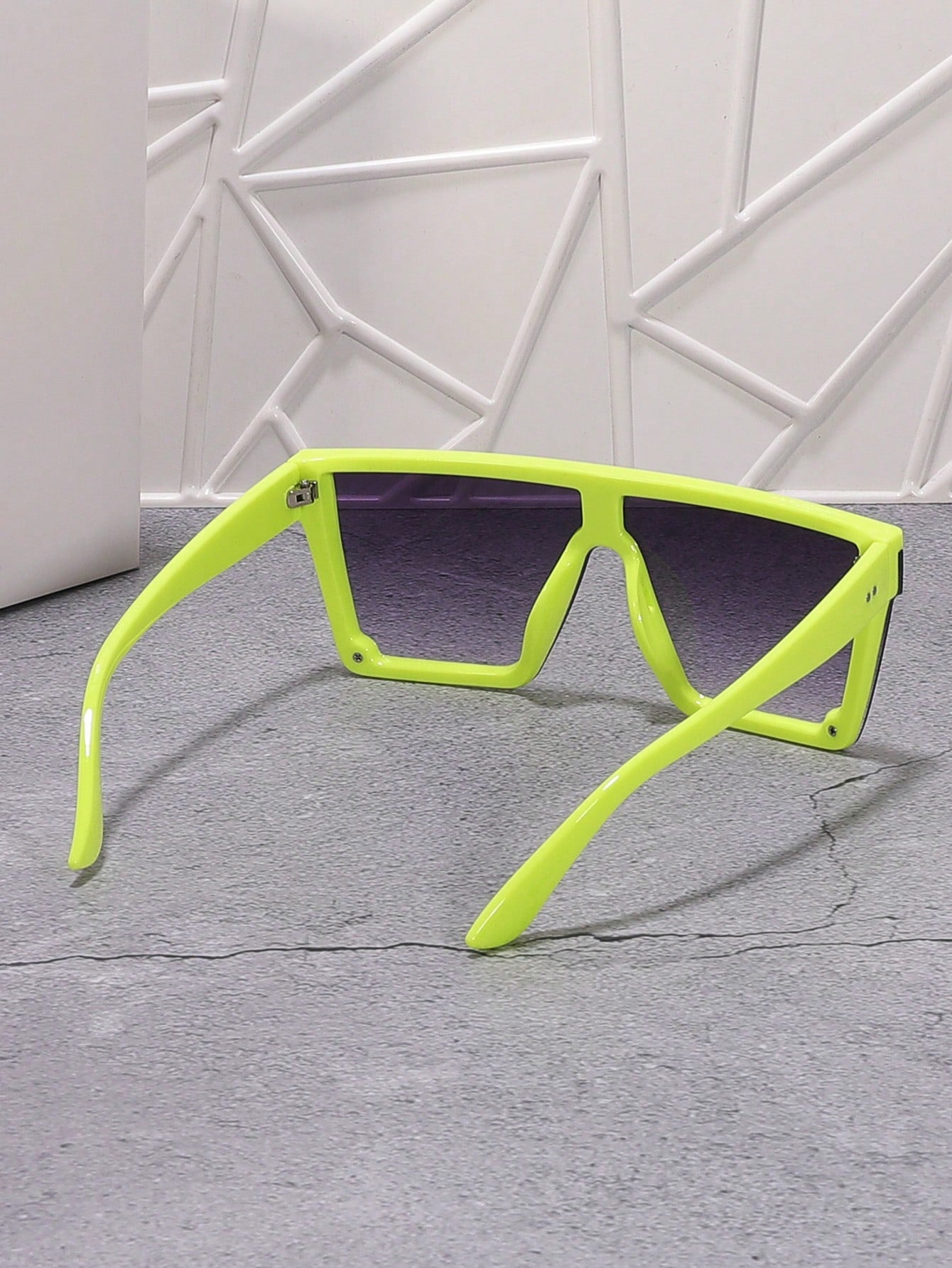 Neon green sunglasses with black lenses on a gray surface with a white geometric wall background