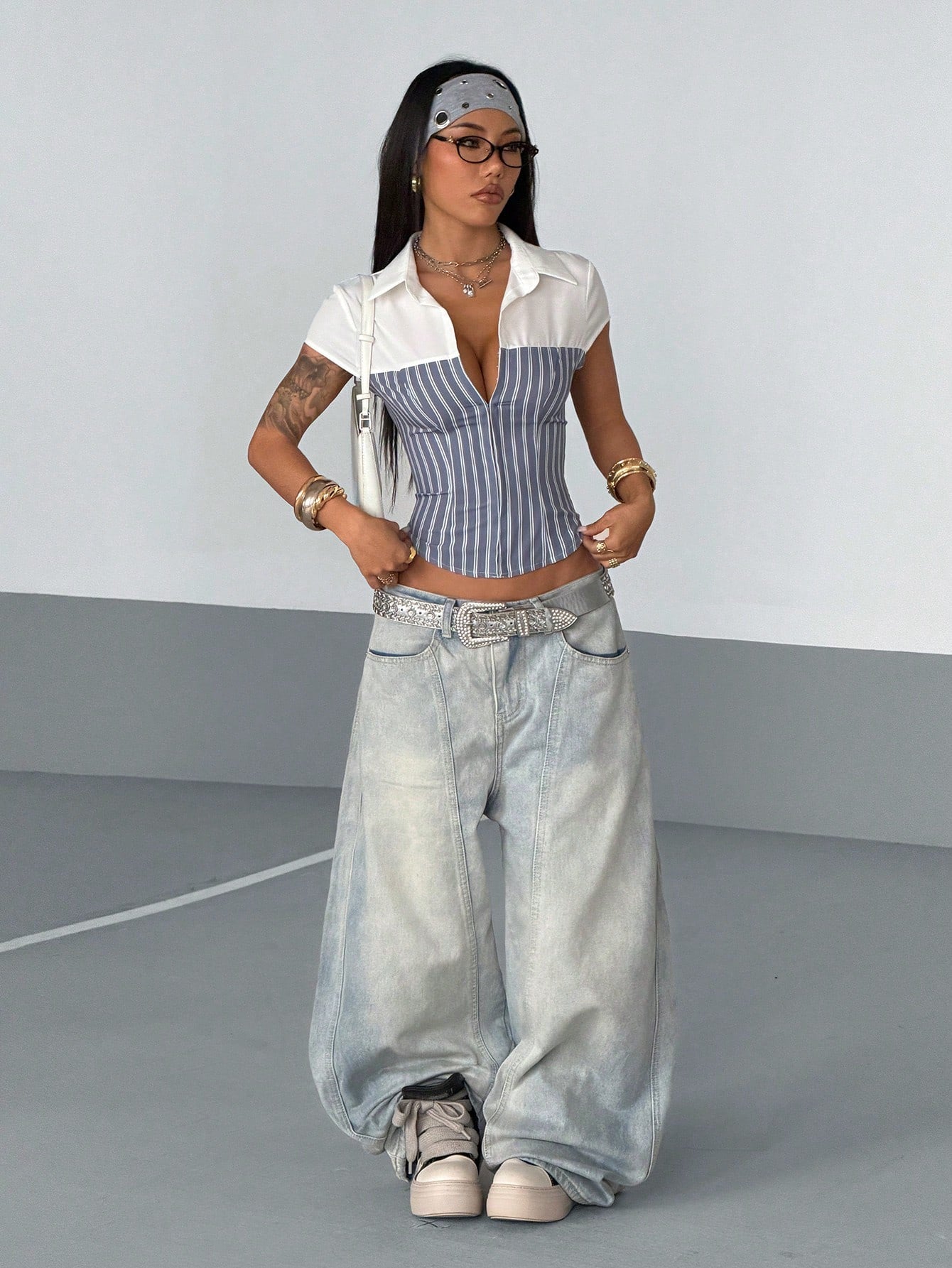 Woman wearing a white shirt, striped top, and wide-leg jeans against a plain background
