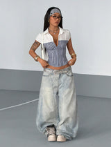 Woman wearing a white shirt, striped top, and wide-leg jeans against a plain background