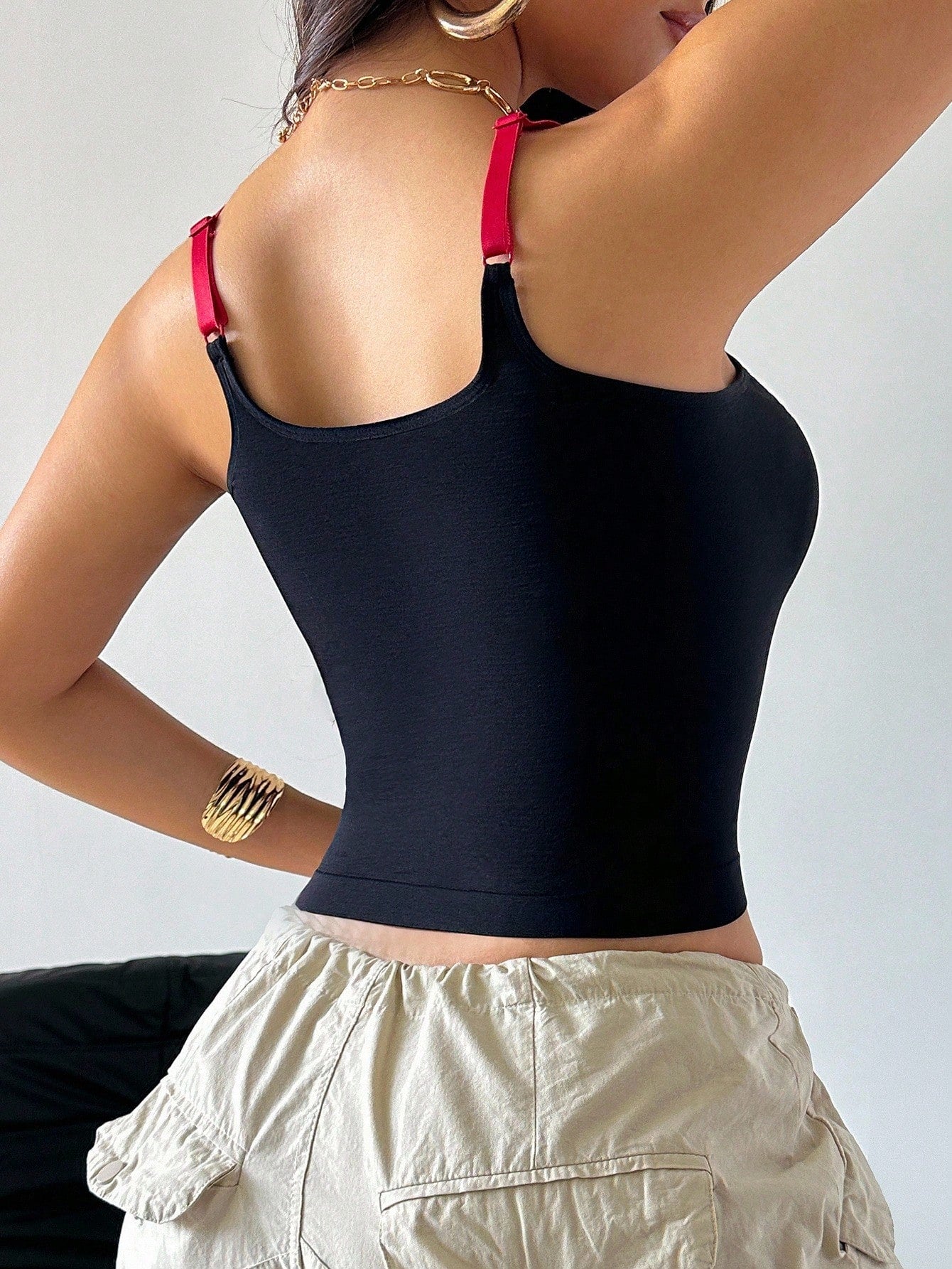 Person wearing a black crop top with red straps and beige pants against a neutral background