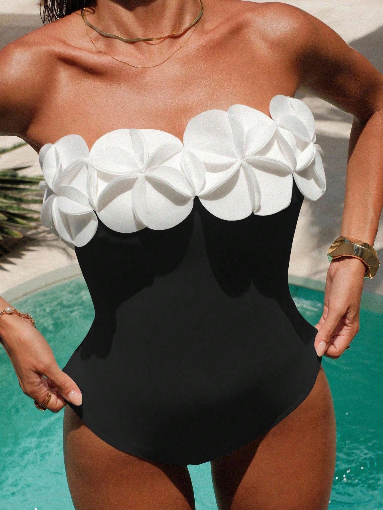 Person wearing a black and white floral one-piece swimsuit by a pool.