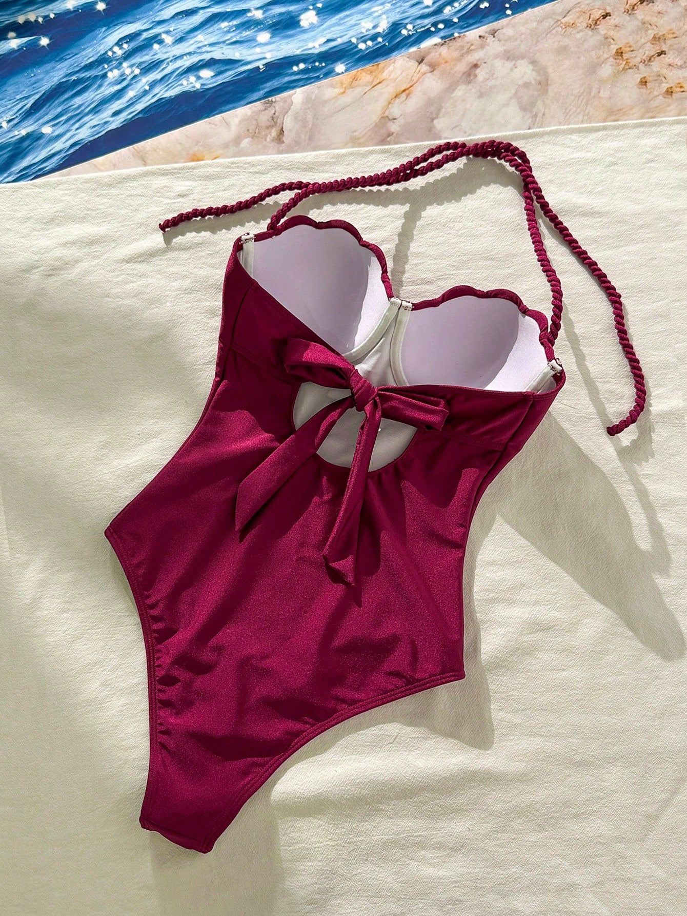 Maroon swimsuit with white accents on a light surface near water.